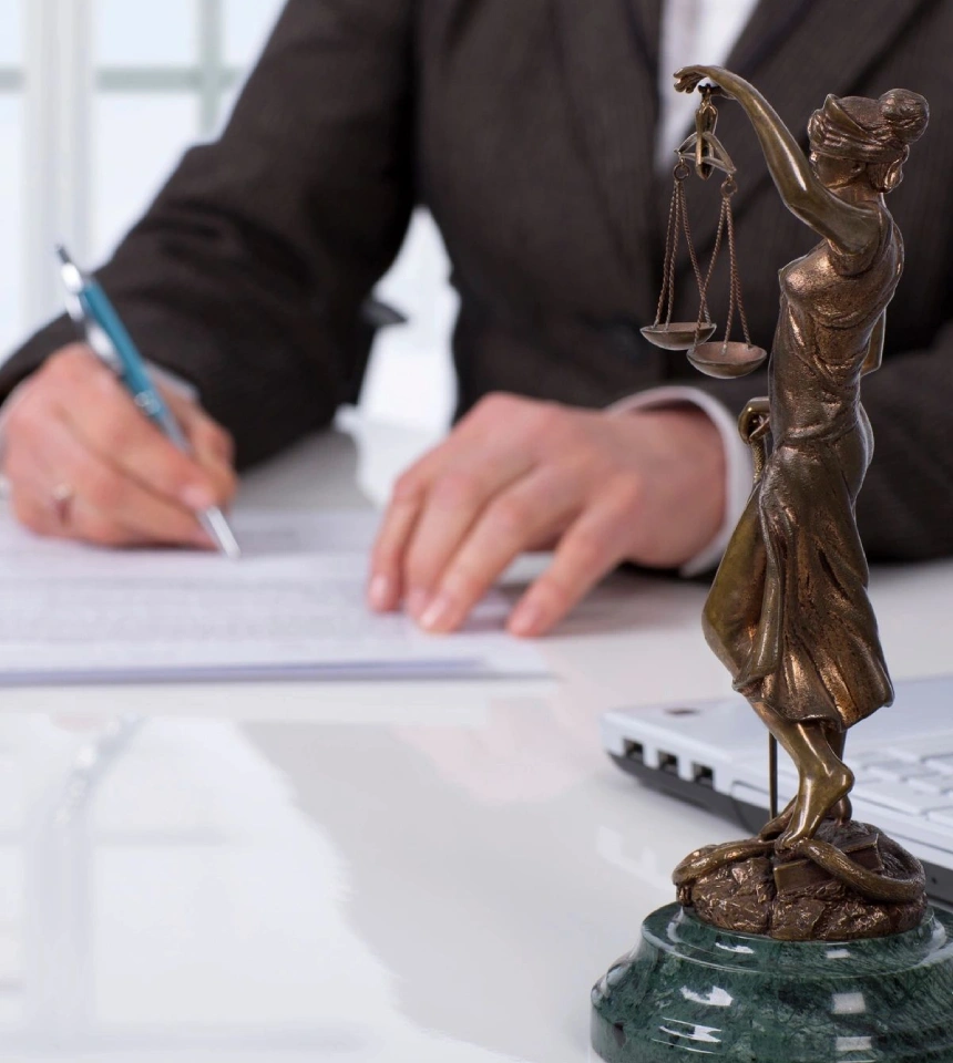 A person writing on paper next to a statue of lady justice.