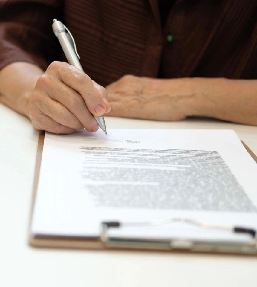 A person writing on paper with pen and clipboard.