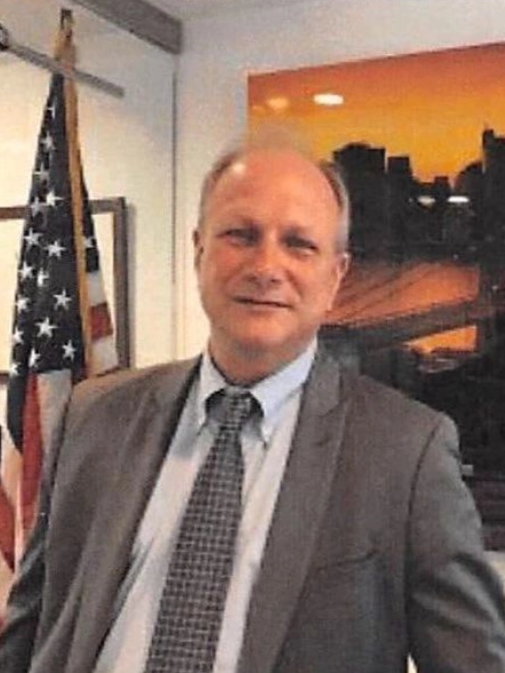 A man in suit and tie standing next to an american flag.